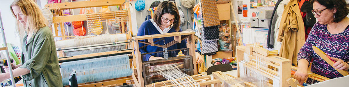 Three women weaving on table looms in a colourful studio
