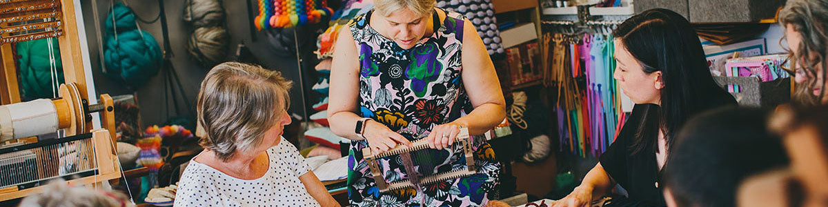 Students watching a weaving teacher weave on a frame loom