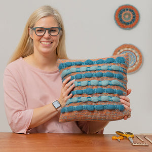 Cassandra Smith smiling and holding up her wool roving cushion designed for her Domesitka online weaving course