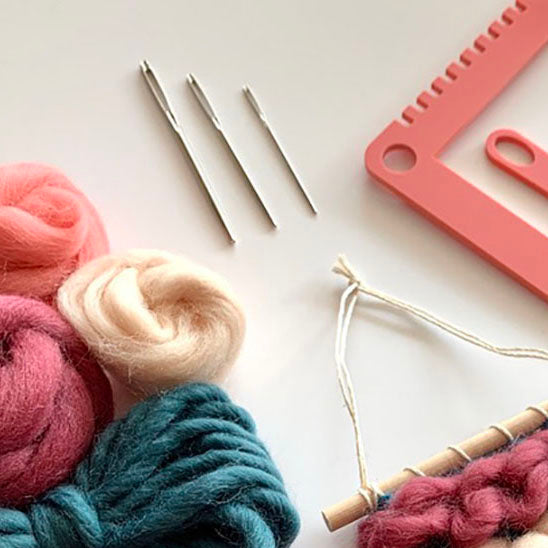 A close up image of 3 Prym tapestry needles laid beside The Oxford Weaving Studio weaving loom and tool set and wool roving fibres