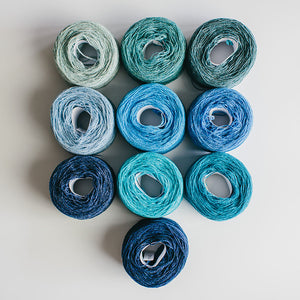 A group of  rainbow-coloured yarn cakes of 2/17s merino lambswool yarn in blues