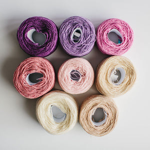 A group of  rainbow-coloured yarn cakes of 2/17s merino lambswool yarn in pinks, purples and neutrals