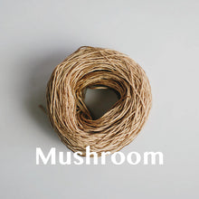 Load image into Gallery viewer, One yarn cake of 4-ply mercerised cotton yarn in mushroom packaged in a compostable plastic bag and an Oxford Weaving Studio sticker