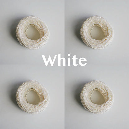 Four yarn cakes of 4-ply mercerised cotton yarn in white packaged in a compostable plastic bag and an Oxford Weaving Studio sticker
