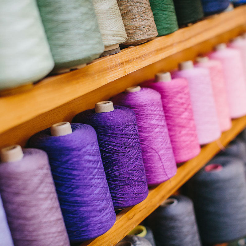 A close up of 2/16s mercerised cotton yarn cones in shades of purple and pink