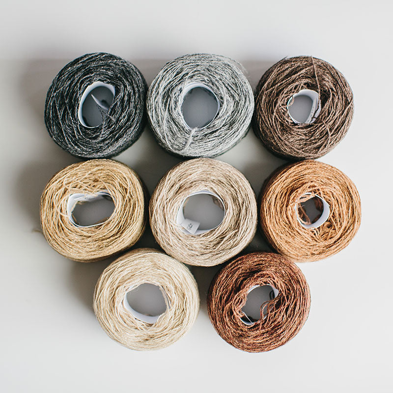 A group of  rainbow-coloured yarn cakes of 2/17s merino lambswool yarn in greys and warm neutrals