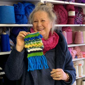 Mature adult smiling and holding up a wall-hanging woven in a workshop at The Oxford Weaving Studio