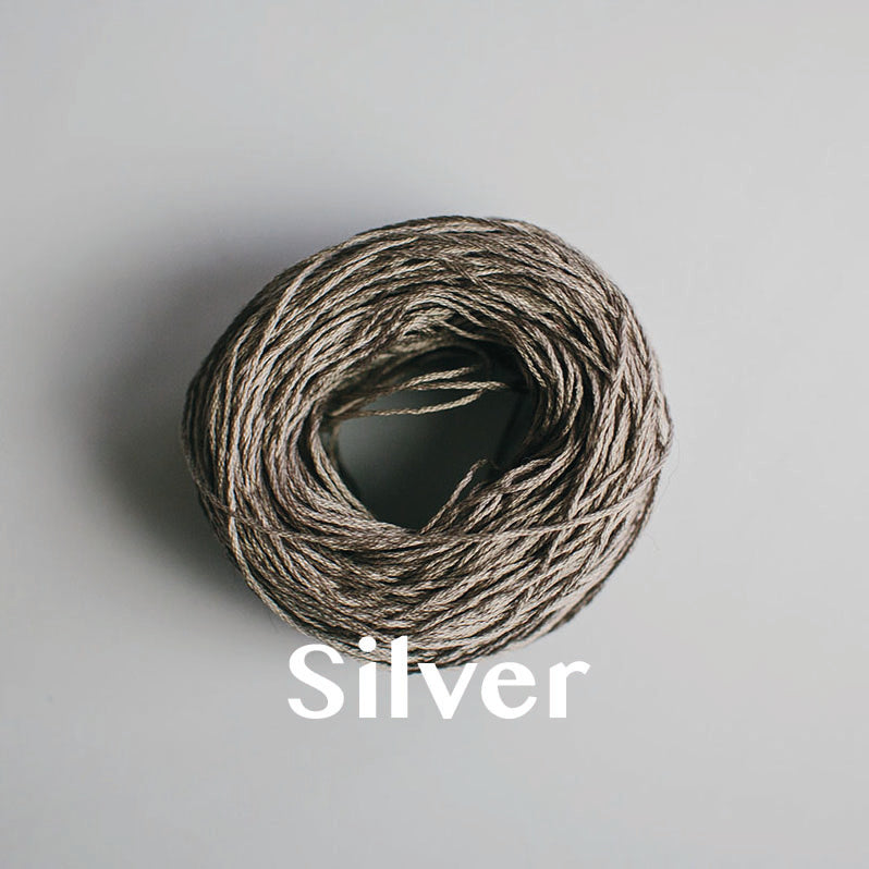 One yarn cake of 4-ply mercerised cotton yarn in silver packaged in a compostable plastic bag and an Oxford Weaving Studio sticker