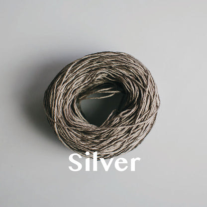 One yarn cake of 4-ply mercerised cotton yarn in silver packaged in a compostable plastic bag and an Oxford Weaving Studio sticker